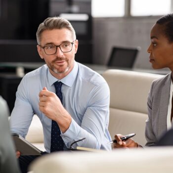 A group of professionals in business attire sitting together in an office for a meeting.